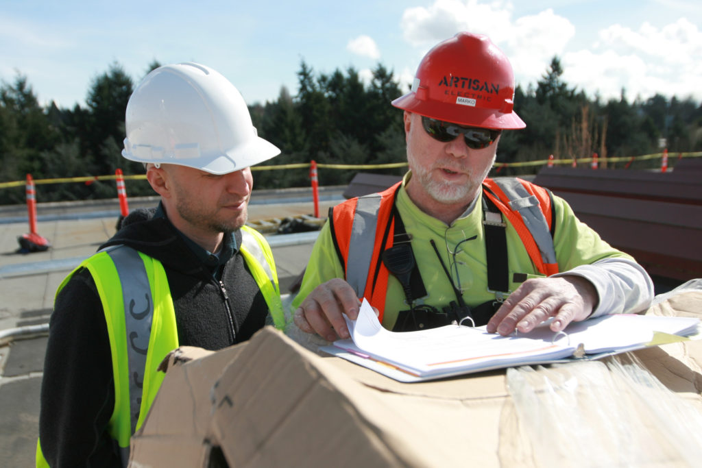 two engineers looking at a chart wearing red and white helmets writing on a paper on a solar installation site